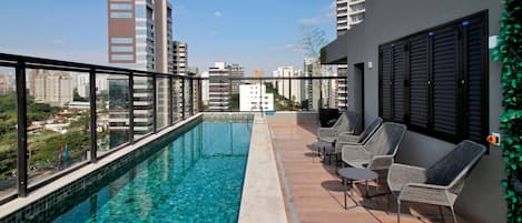 A rooftop pool with clear blue water, surrounded by a wooden deck and wicker chairs.