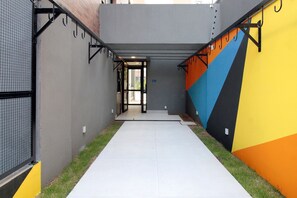 A narrow corridor with a tiled floor, a metal railing on one side, and a colorful wall on the other. - Boulevard Agami (São Paulo)