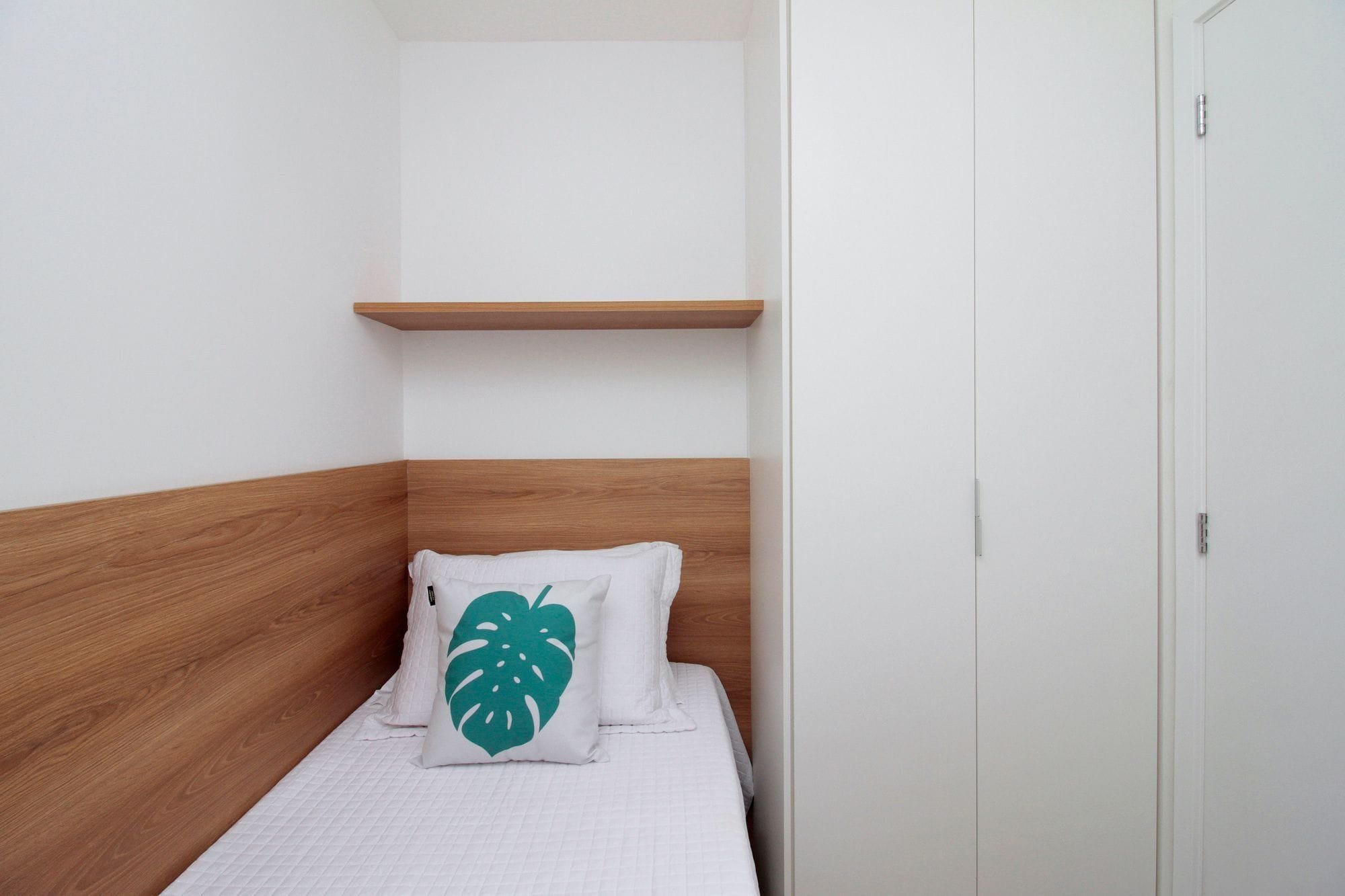 A single bed with a wooden headboard, a white wall, and a white door.