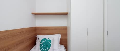 A single bed with a wooden headboard, a white wall, and a white door.