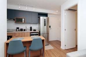 A compact kitchen with modern appliances, a dining area with two chairs, and a white door leading to another room. - Boulevard Agami (São Paulo)