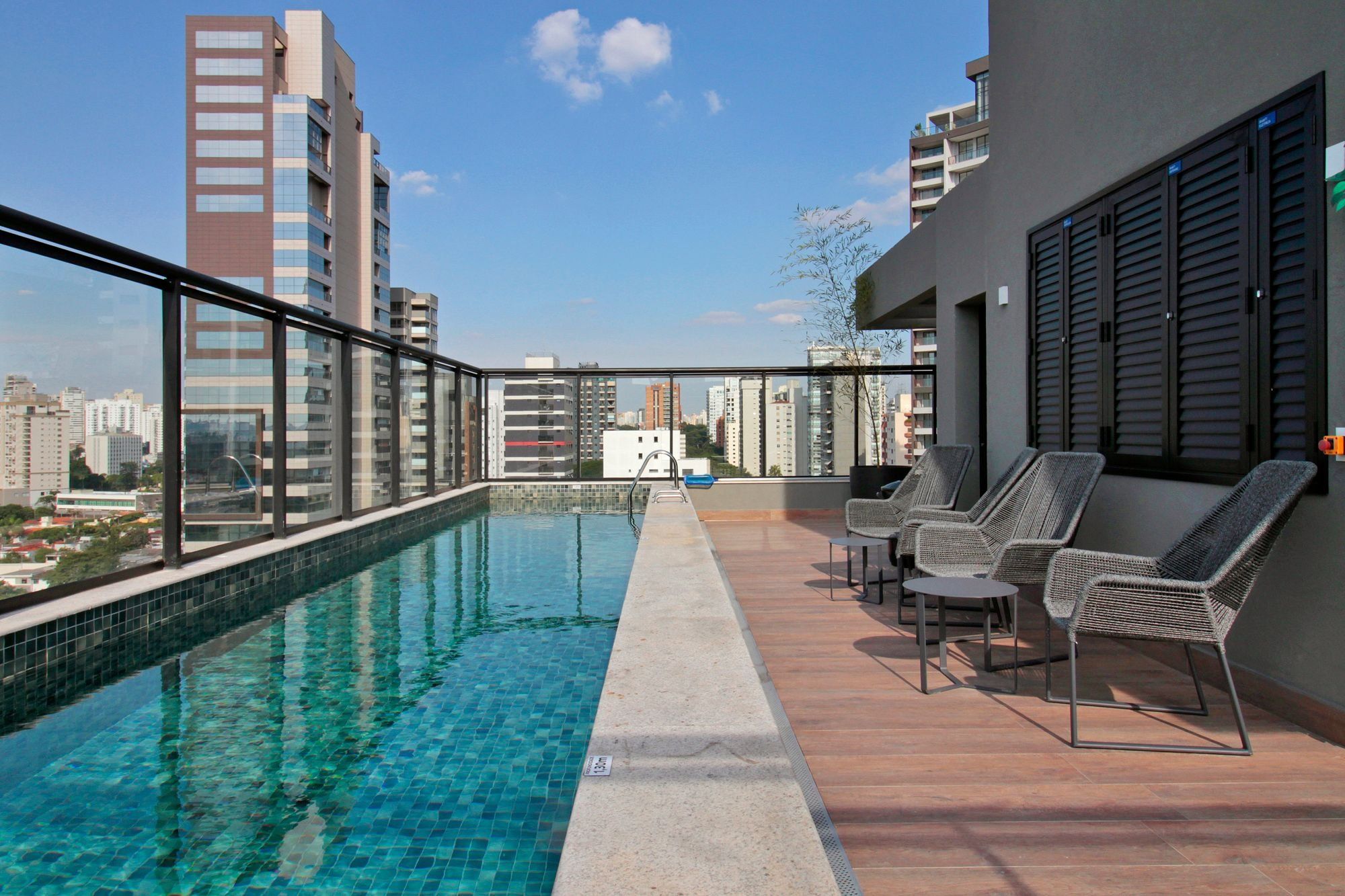 A rooftop pool with clear blue water, surrounded by high-rise buildings, and furnished with wicker chairs.