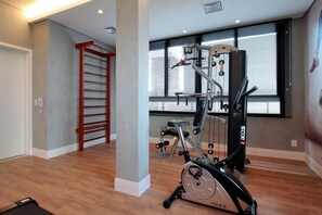 A gym with a stationary bike, a pull-up bar, and a window with blinds. - Boulevard Agami (São Paulo)