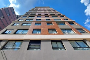 A high-rise building with a modern architectural design, featuring a mix of brick and concrete facades, multiple windows, and a clear sky in the background. - Boulevard Agami (São Paulo)