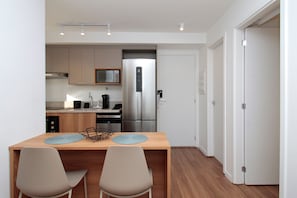 A compact kitchen with a microwave, coffee maker, and stainless steel refrigerator. There is a wooden dining table with two chairs.