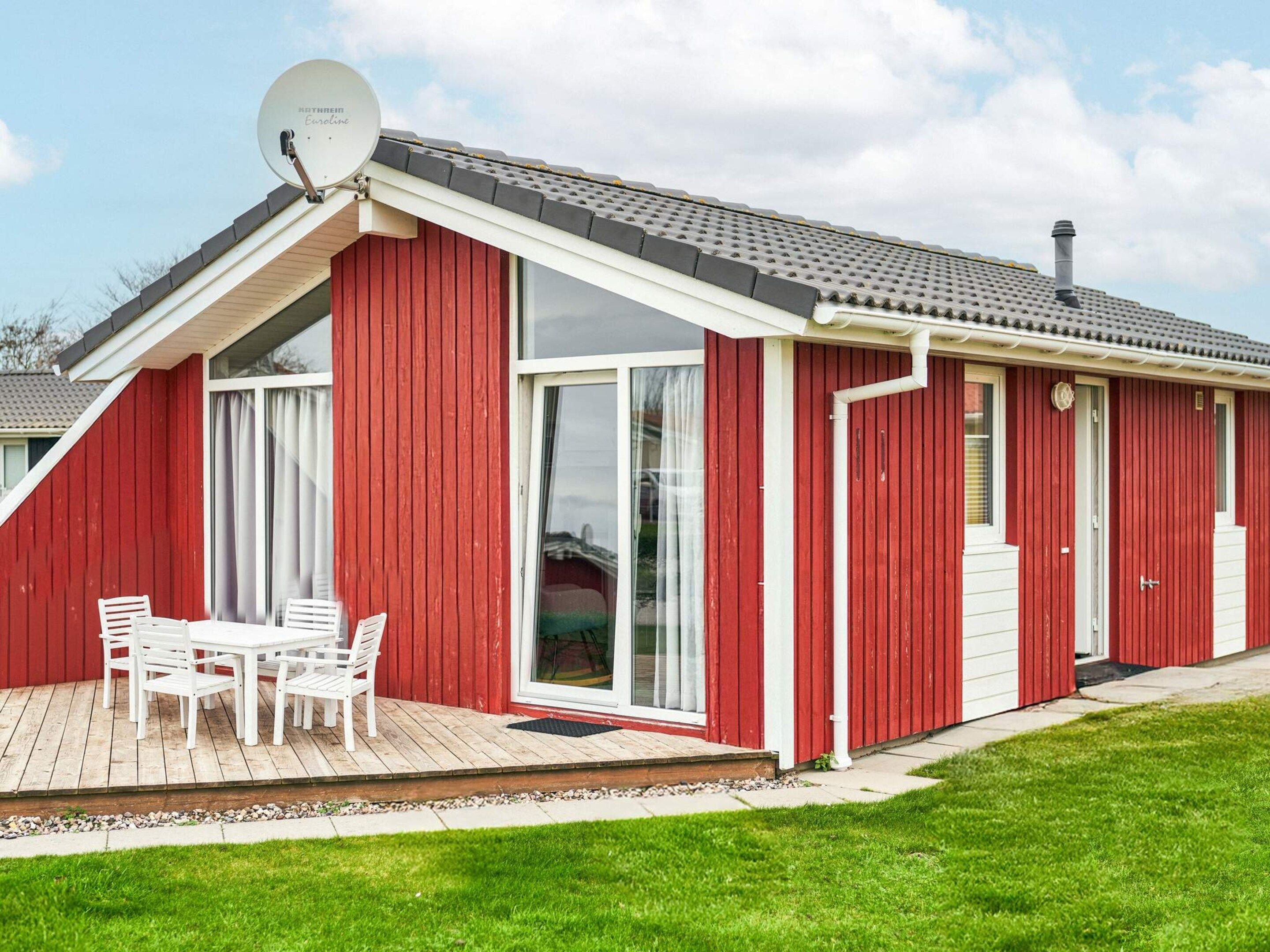 A red building with a sloped roof, a satellite dish, and a patio with a table and chairs.