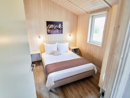 Une petite chambre à coucher accueillante, avec un plafond en bois, un lit simple avec une literie blanche, une table de chevet et une fenêtre.