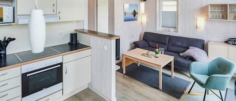 Una cocina moderna con horno empotrado, un comedor con mesa y sillas, y una sala de estar con sofá y televisión.