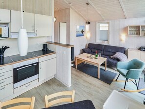 Una cocina moderna con horno empotrado, un comedor con mesa y sillas, y una sala de estar con sofá y televisión.