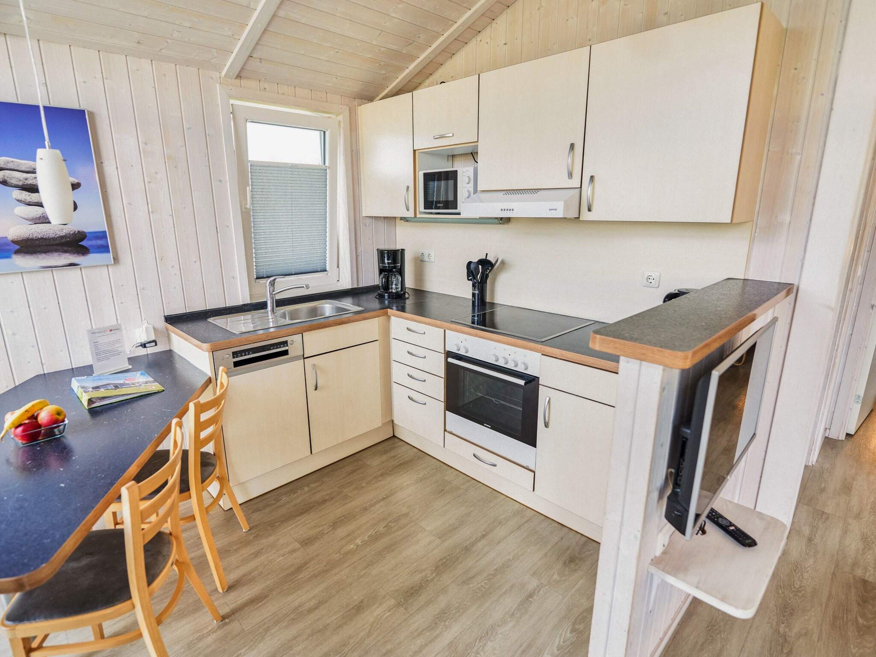 A compact kitchen with a microwave, stove, and sink. There is a dining table with chairs and a small window.