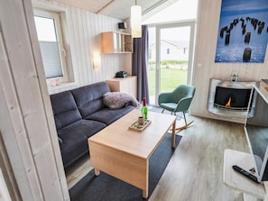 A modern living room with a sofa, a coffee table, a fireplace, and a view of the outdoors. - 4 Star Holiday Home in Friedrichkoog (Friedrichskoog)