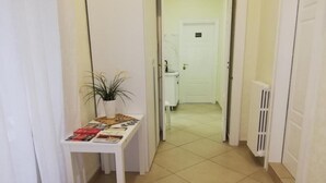 Un pasillo con una mesa blanca que muestra revistas, una planta en maceta y una puerta que da al baño.