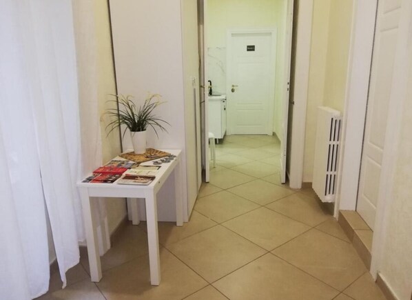 Un couloir avec une table blanche où sont exposés des magazines, une plante en pot et une porte donnant accès à une salle de bain.