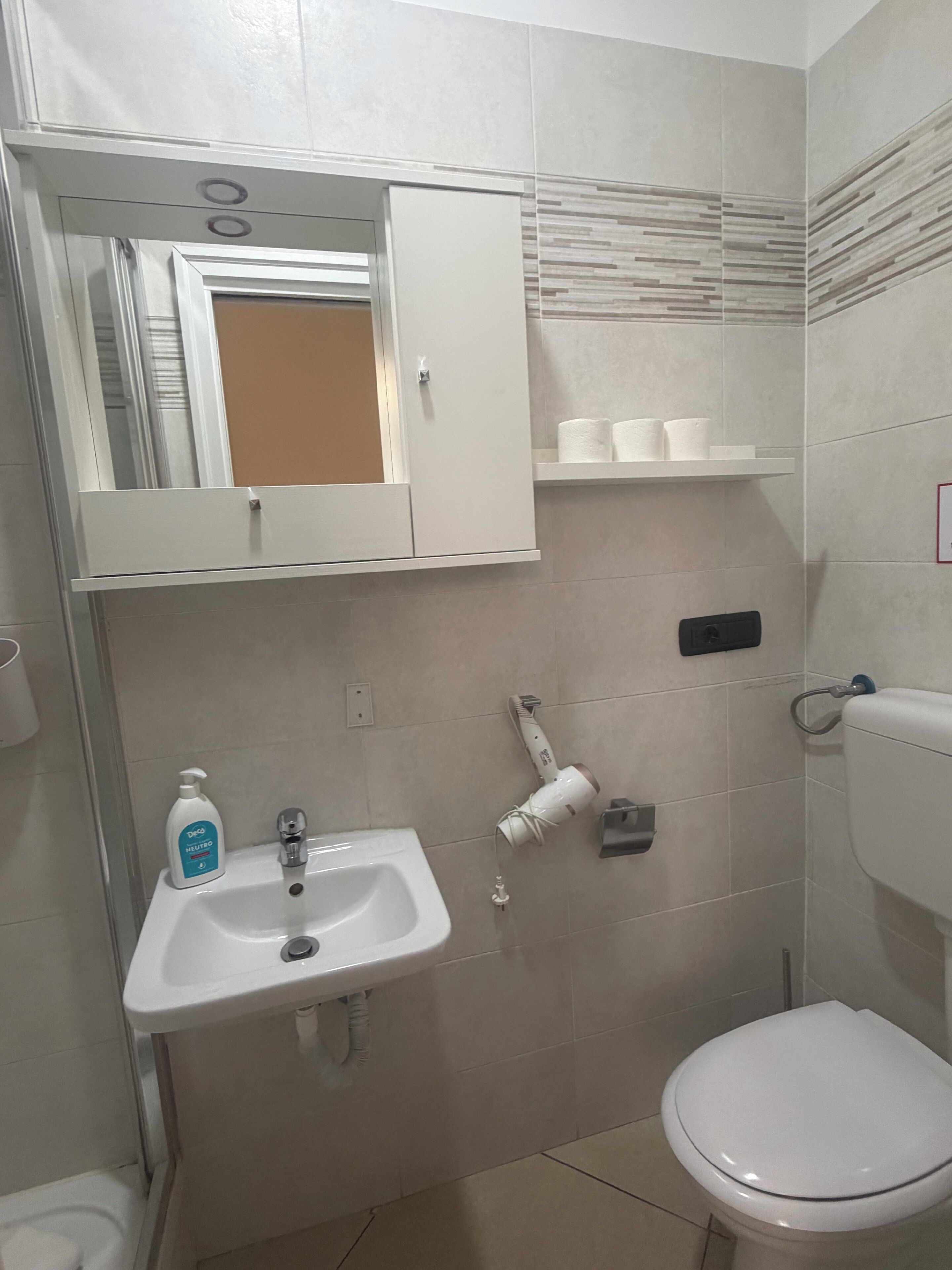 Un baño con un lavamanos blanco, un inodoro y un espejo sobre el lavamanos.