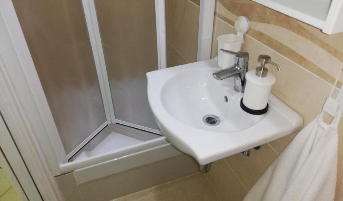 Un baño con lavamanos blanco, ducha y toallero.