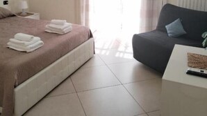 Una habitación de hotel con cama, sofá, una mesita y televisor en la pared.