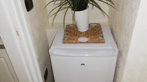 Un electrodoméstico pequeño y blanco, posiblemente un refrigerador o congelador, con un felpudo tejido y una planta en maceta encima.
