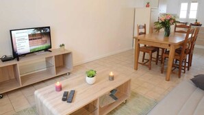 Un salon moderne avec un téléviseur, des meubles en bois et une petite table agrémentée d’une plante et d’une bougie.