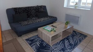 Un salon avec un canapé, une table basse, une petite plante et une fenêtre avec des rideaux.