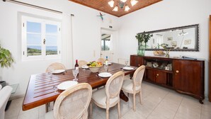 A dining area with a wooden table, wicker chairs, a fruit bowl, wine glasses, and a wooden cabinet with a mirror.