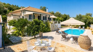 A villa with a swimming pool, outdoor seating, and a stone pathway.