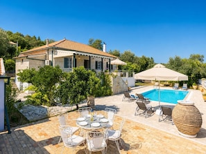 A villa with a swimming pool, outdoor seating, and a stone pathway.