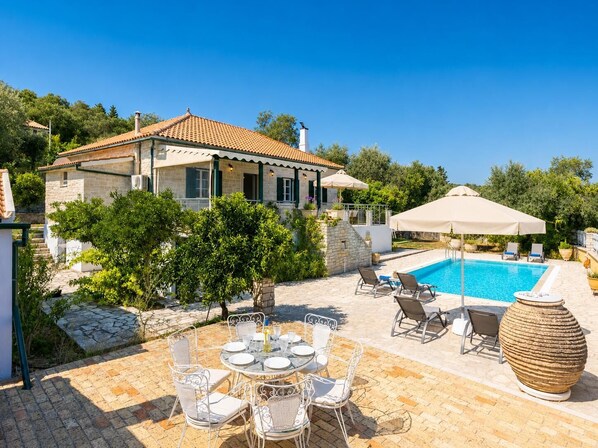 A villa with a swimming pool, outdoor seating, and a stone pathway. - Villa Afroditi - Three Bedroom Villa, Sleeps 6 (Kourteika)