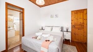 A bedroom with a bed, bedside tables, a wooden door, and a bathroom visible through an open door.
