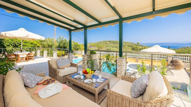 A covered outdoor seating area with wicker furniture, a pool, and a view of the sea.
