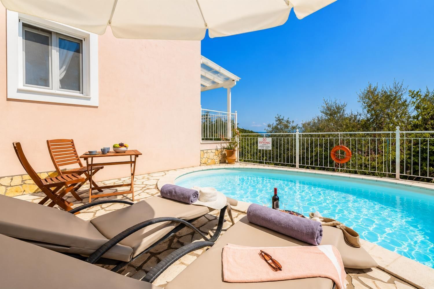 Zona de piscina con sillones de descanso, una mesa con frutero y señal de advertencia para buceo.