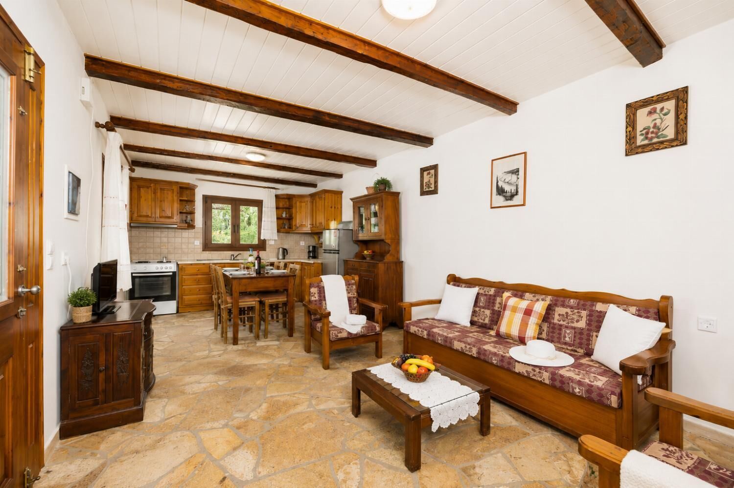 A spacious living area with a stone floor, wooden furniture, a sofa with patterned cushions, and a dining table.