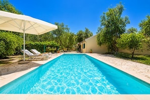 A rectangular swimming pool with clear blue water, surrounded by a stone deck. There are lounge chairs and a white umbrella. - Villa Old Vineyard - One Bedroom Villa, Sleeps 2 (Paxi)