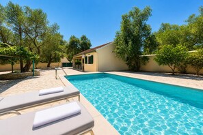 Une piscine avec des chaises longues, un espace abrité et des arbres.
