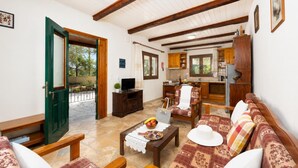 A living room with a sofa, coffee table, and TV, a dining area with chairs, and a kitchen with wooden cabinets. - Villa Old Vineyard - One Bedroom Villa, Sleeps 2 (Paxi)