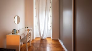 A room with a glass desk, a round mirror, a white chair, a small plant, and a white curtain.