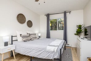 Une chambre moderne avec un lit, des tables de chevet, un bureau, une télévision et une fenêtre avec des rideaux.