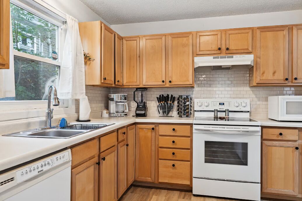 A kitchen with wooden cabinets, a white stove, a microwave, and a coffee maker.