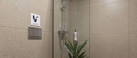A modern bathroom with a glass-enclosed shower, a toilet, a small trash bin, and a potted plant.