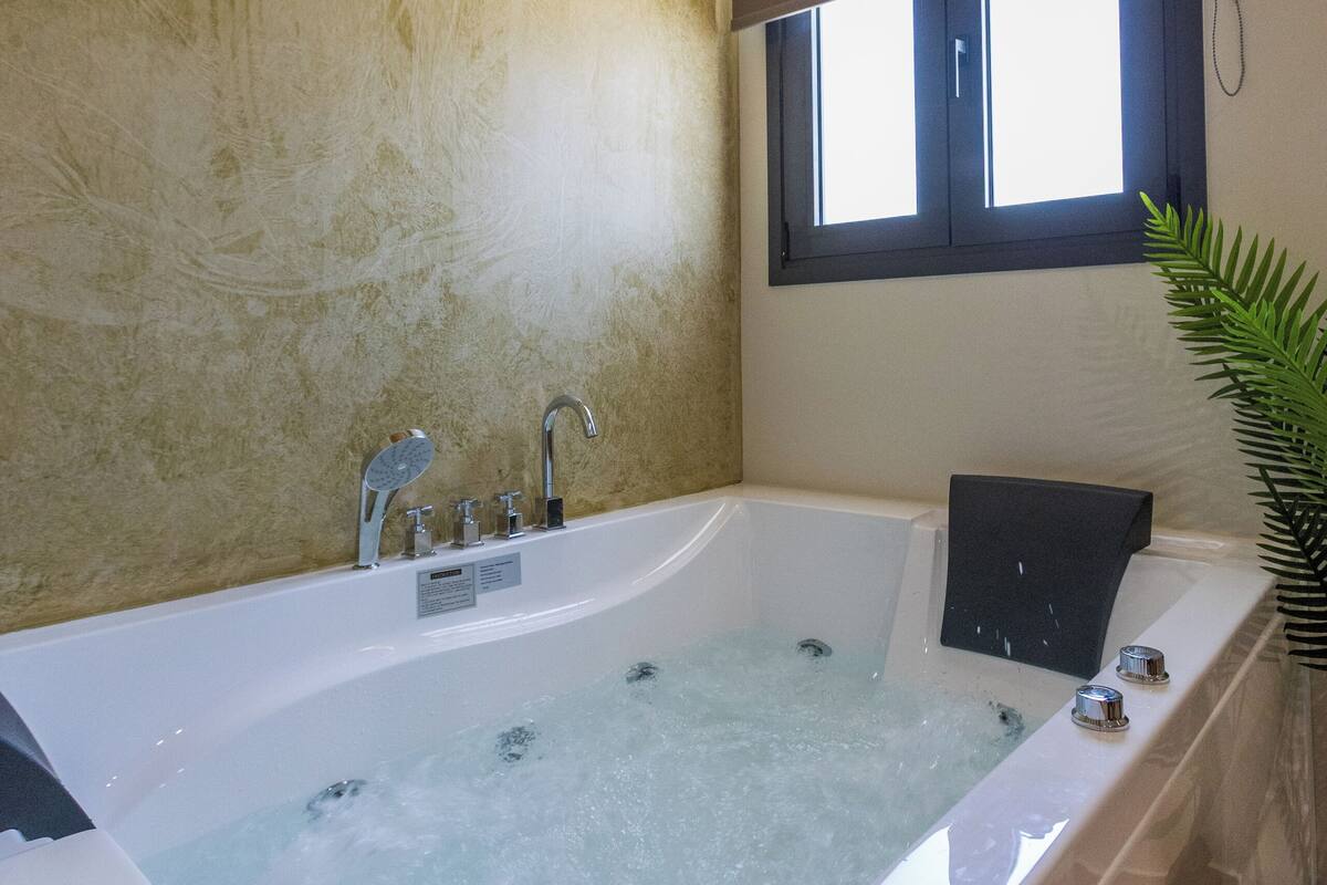 Une salle de bain moderne avec une grande baignoire, des poutres en bois au plafond, une fenêtre et une plante en pot.