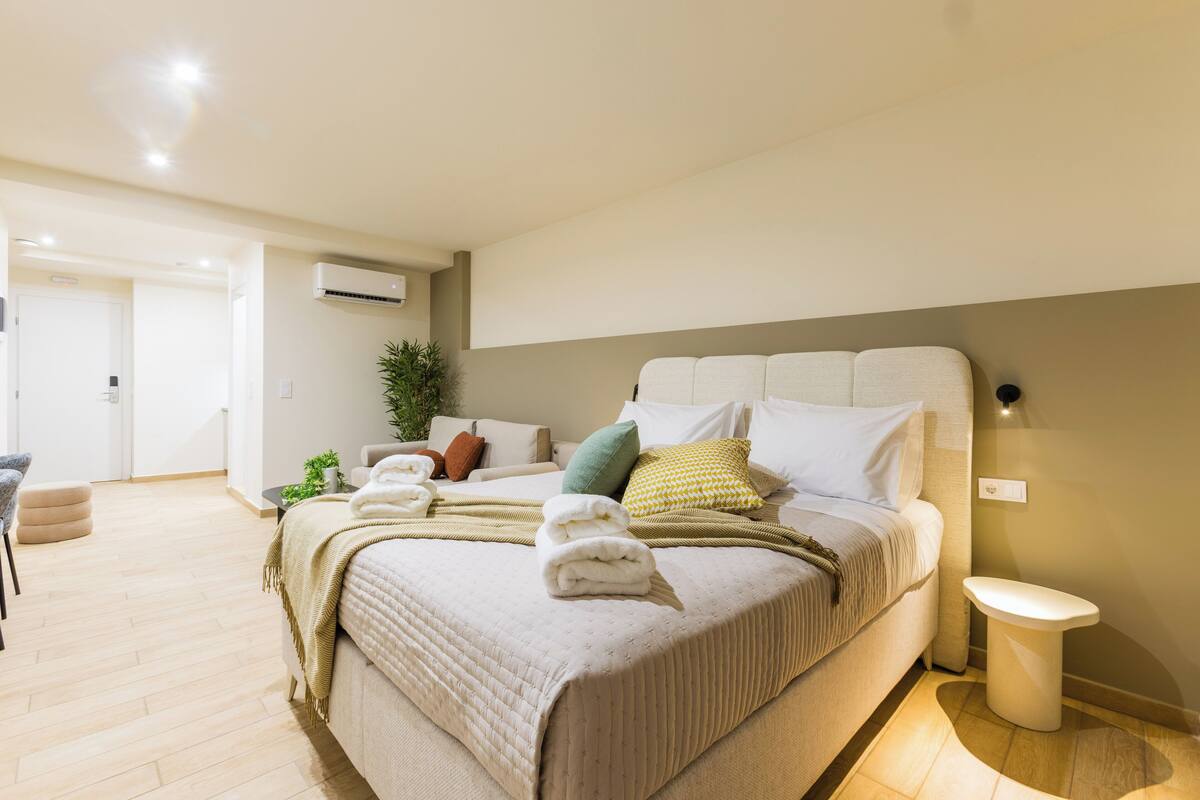 Une chambre à coucher bien rangée, avec un lit, une table de chevet et un petit tabouret.