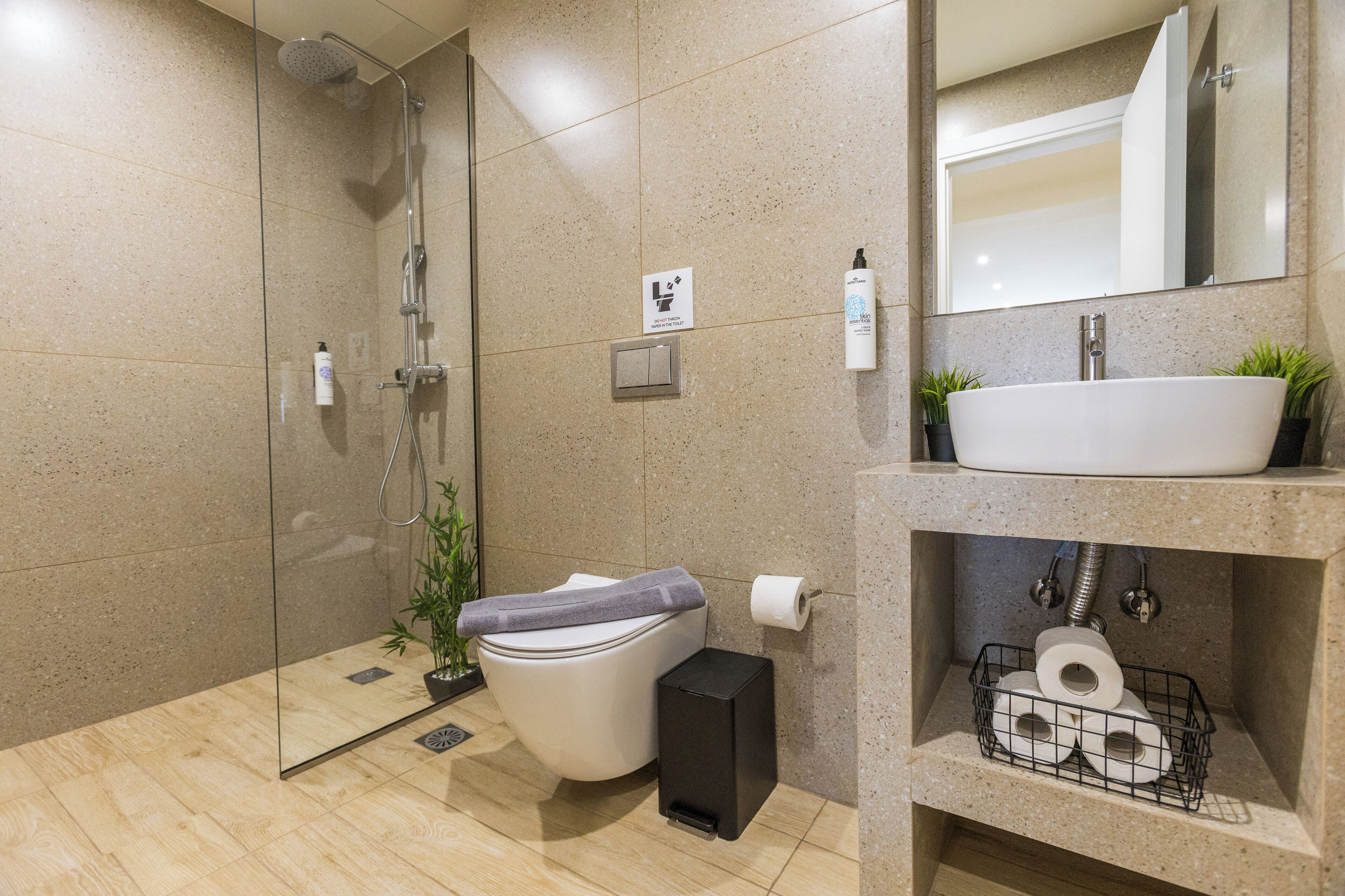 Un bany modern amb dutxa de vidre, vàter i un lavabo amb plantes.