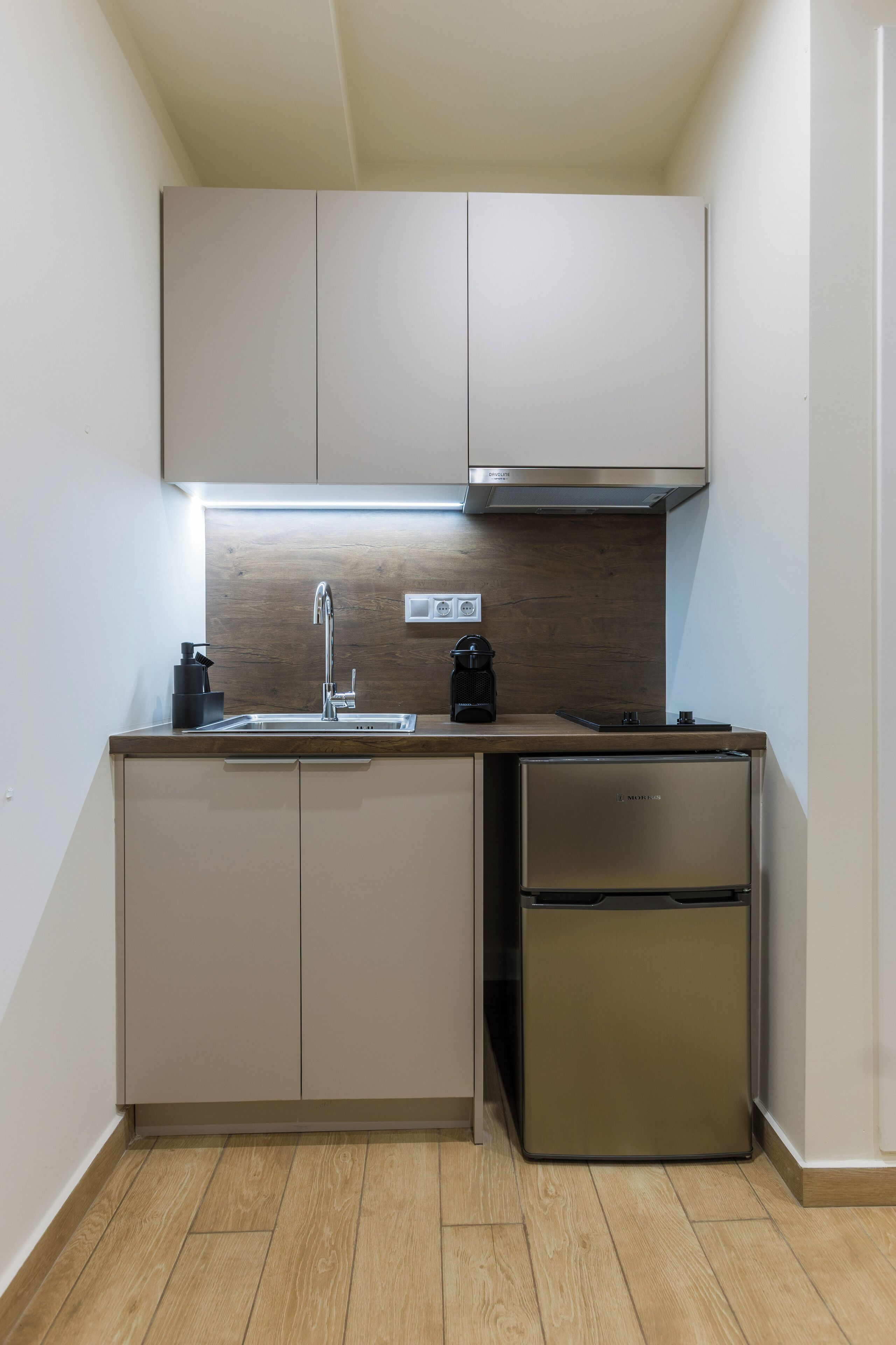 Una cocina compacta con un refrigerador de acero inoxidable, un lavamanos y una cafetera.