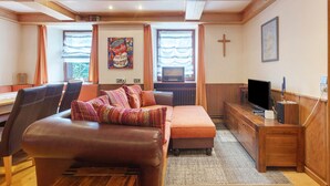 Ein gemütliches Zimmer mit einem braunen Ledersofa, einem Holztisch, einem Fernseher und einem Kreuz an der Wand.