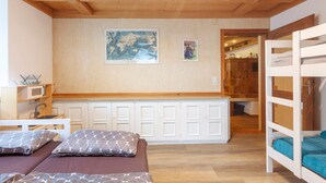 Ein Zimmer mit Etagenbetten, Holzboden, einer Küchenzeile und einer Wand mit zwei gerahmten Bildern.