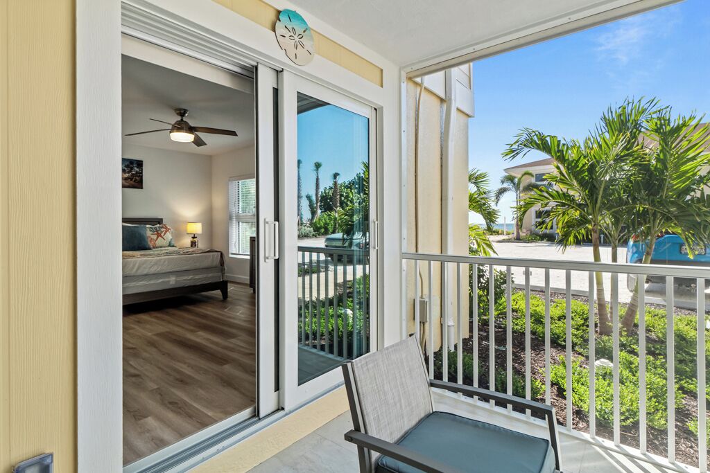 A balcony with a view of a residential area, a sliding glass door leading to a bedroom, and a ceiling fan.
