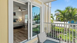 A balcony with a view of a residential area, a sliding glass door leading to a bedroom, and a ceiling fan.