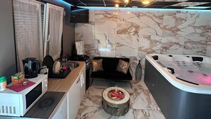 A compact, modern kitchen with a microwave, kettle, and coffee maker. A small dining area with a round table and a sofa is visible. - Ô Saphir Spa - House N2 (Denain)