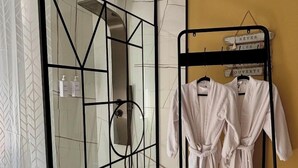 A bathroom with a glass shower enclosure, a towel rack with robes, and toiletries on the wall. - Ô Saphir Spa - House N2 (Denain)