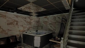 A spa room with a hot tub, a sofa, a small table, and a staircase. - Ô Saphir Spa - House N2 (Denain)