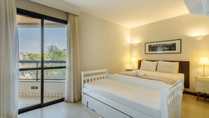 Une chambre d’hôtel avec un lit, une table de chevet, une lampe, un tableau encadré au mur et une vue par la fenêtre.